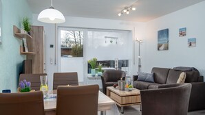 Un salon moderne avec un coin repas, comprenant un canapé, des fauteuils, une table basse et un luminaire suspendu.