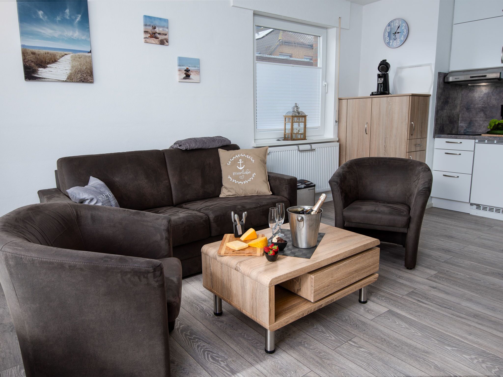 Un salon moderne avec un canapé marron, une table basse en bois sur laquelle se trouvent des plats et des boissons, et une cuisine en arrière-plan.