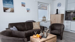 Un salon moderne avec un canapé marron, une table basse en bois sur laquelle se trouvent des plats et des boissons, et une cuisine en arrière-plan.