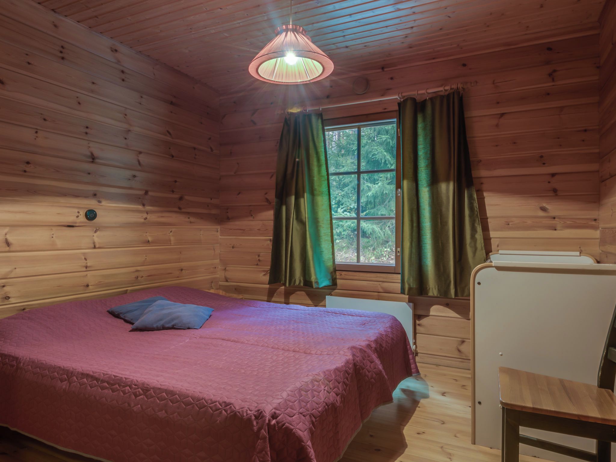 Ein Zimmer in einer Holzhütte mit einem Bett, einem Schreibtisch und einem Fenster mit Vorhängen.