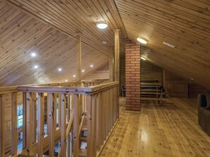 A wooden interior with a high ceiling, a brick fireplace, and a wooden staircase.