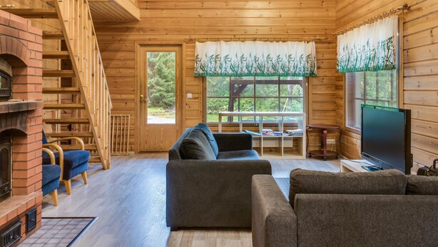 Un intérieur de chalet chaleureux avec une cheminée, un escalier en bois, des sièges confortables et un téléviseur.