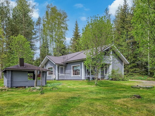 A two-story house with a sloped roof, surrounded by a well-maintained lawn and dense forest.