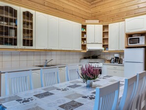 Una cocina con armarios blancos, estufa, microondas y una mesa de comedor con sillas.