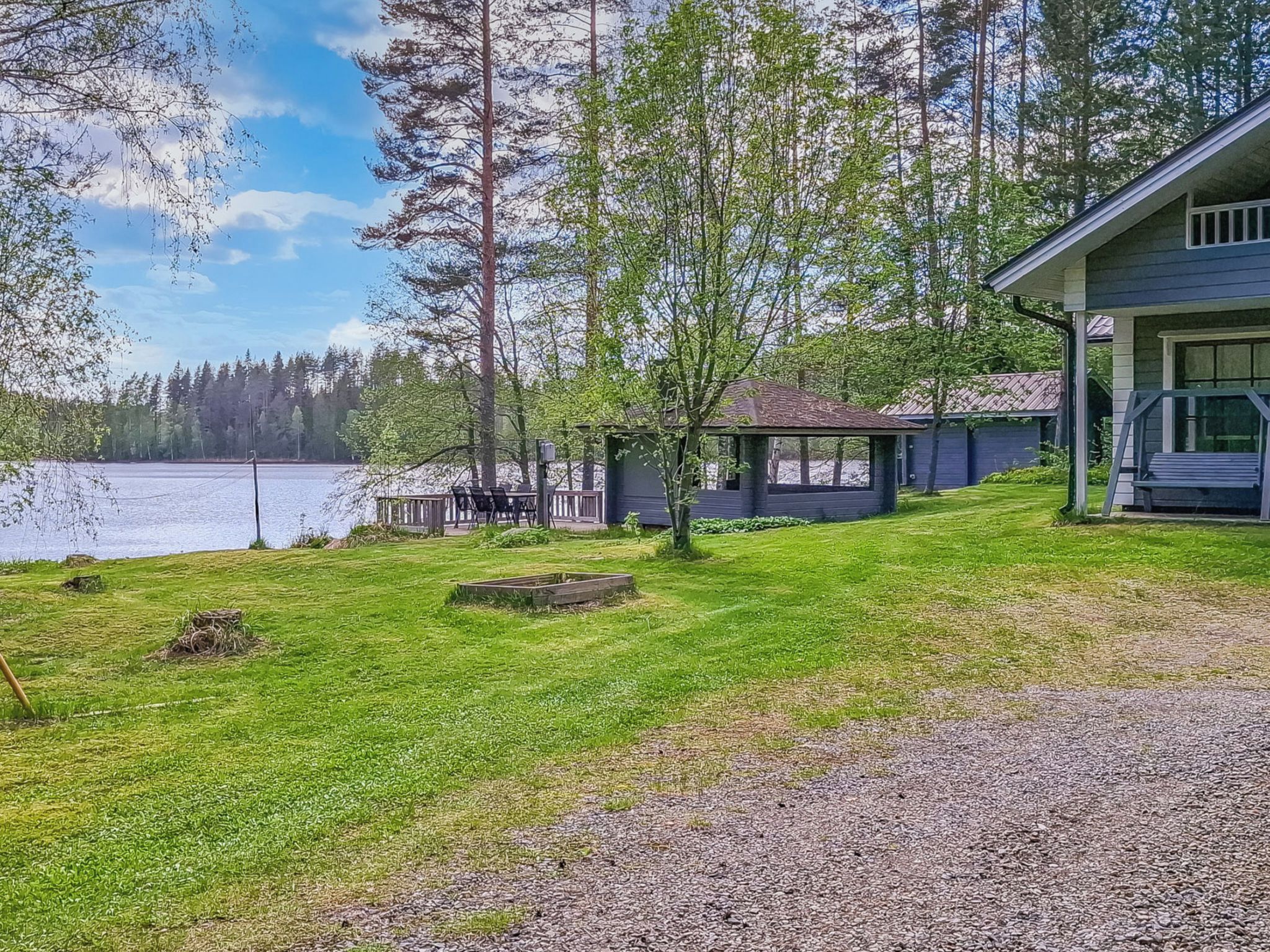 Järvenrantatontti, jossa on nurmikko, puinen terassi ja kuistilla varustettu rakennus.