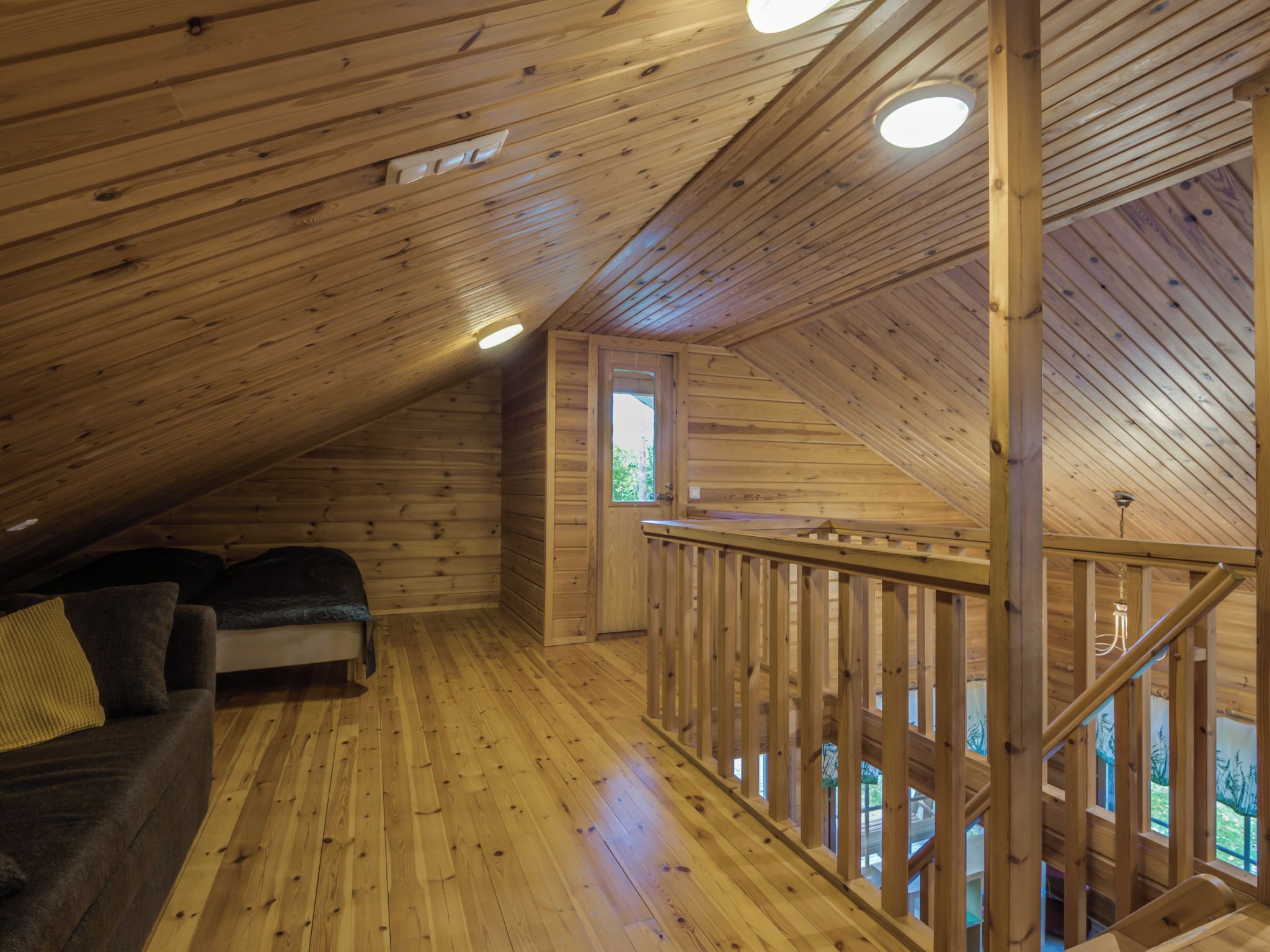 Un interior de madera con techo inclinado, un sofá y una escalera.