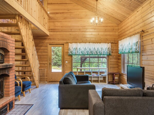 A wooden cabin interior with a fireplace, a sofa, a television, and a staircase.