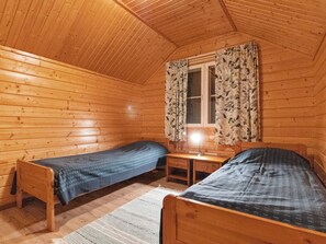 Una baita con due letti di legno, un tavolino, una finestra con tende e un soffitto in legno.