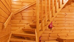 Una escalera de madera con barandilla, un pequeño banco y un extintor de incendios en la pared.