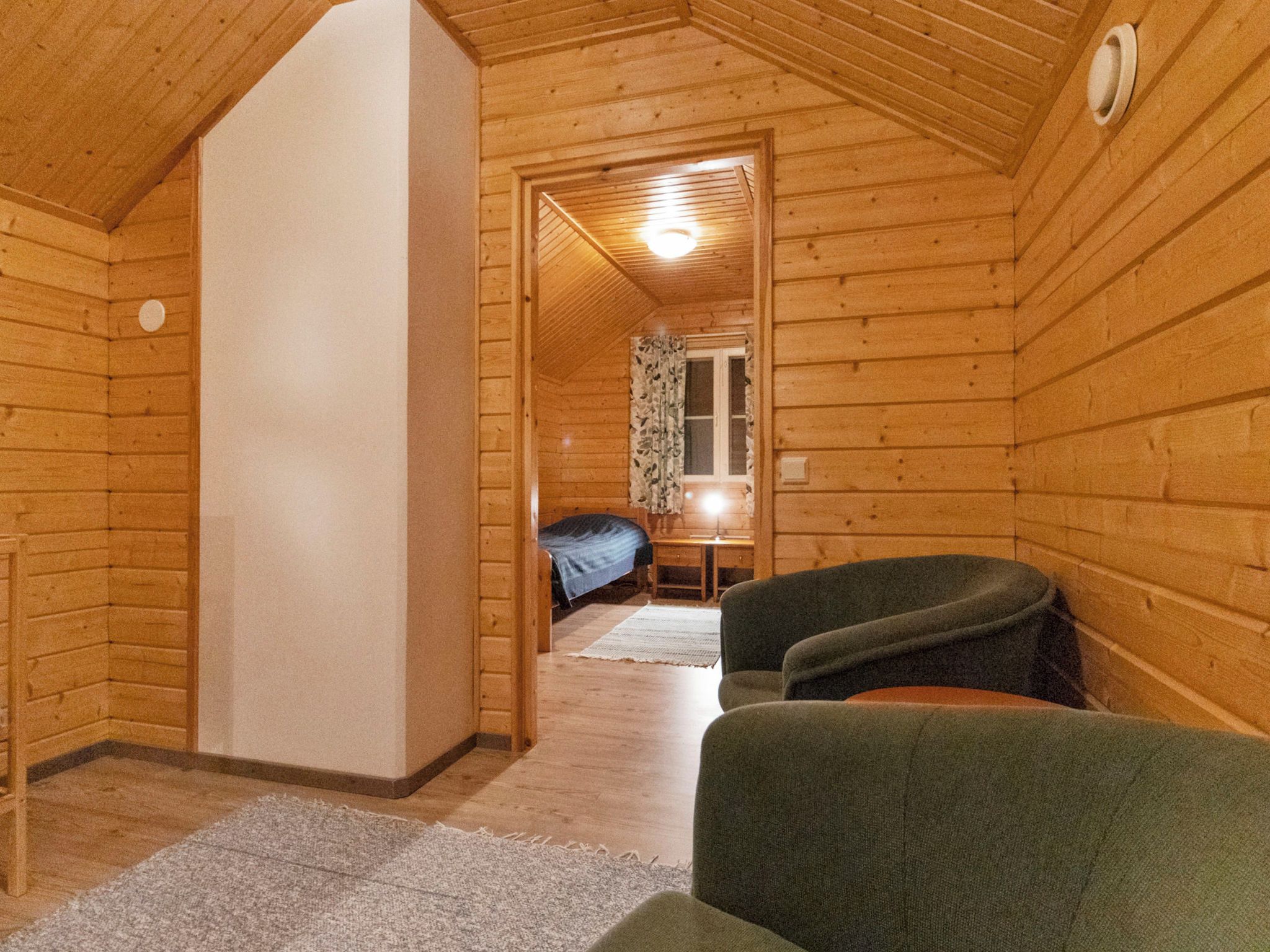 A cozy cabin interior with a wooden ceiling, a bed, a desk, and a chair.