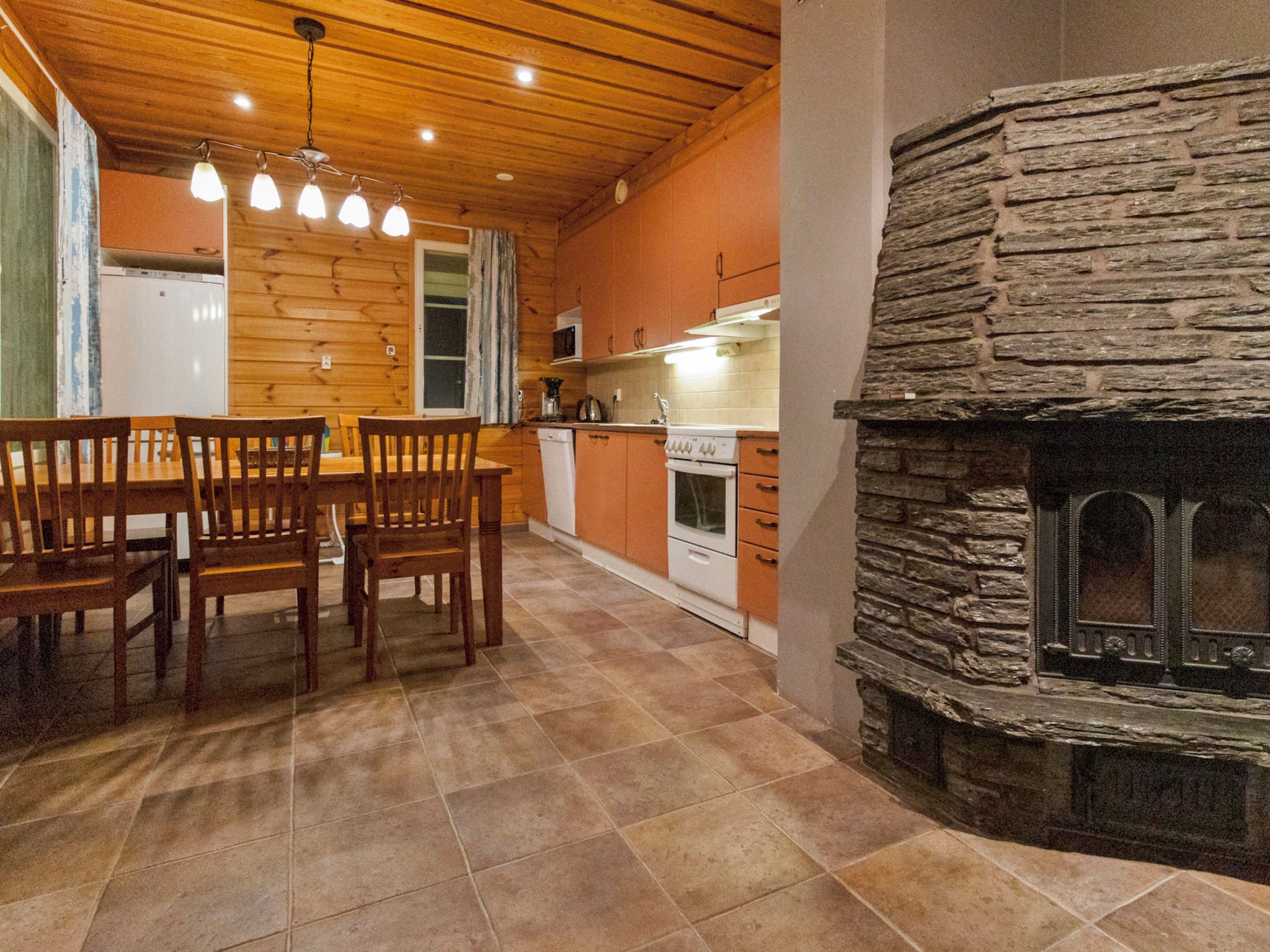 A kitchen with wooden cabinets, a stone fireplace, and a dining table with chairs.