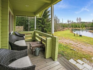 A covered porch with wicker furniture and a table, overlooking a lake and forest. - Metsämökki by Interhome (Raasepori)