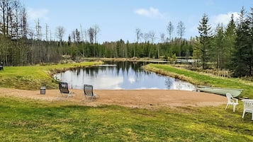 Rauhallinen paikka järven rannalla, jossa on vene, tuoleja ja pieni laituri.