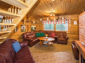 Interior de una cabaña de troncos con escalera de madera, mobiliario de cuero y decoración de cuernos de ciervo.