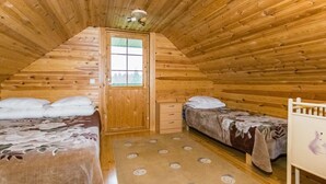 A cozy attic bedroom with wooden walls and a sloped ceiling. There are two beds with floral bedding, a small wooden dresser, and a door leading outside. - Metsämökki by Interhome (Raasepori)