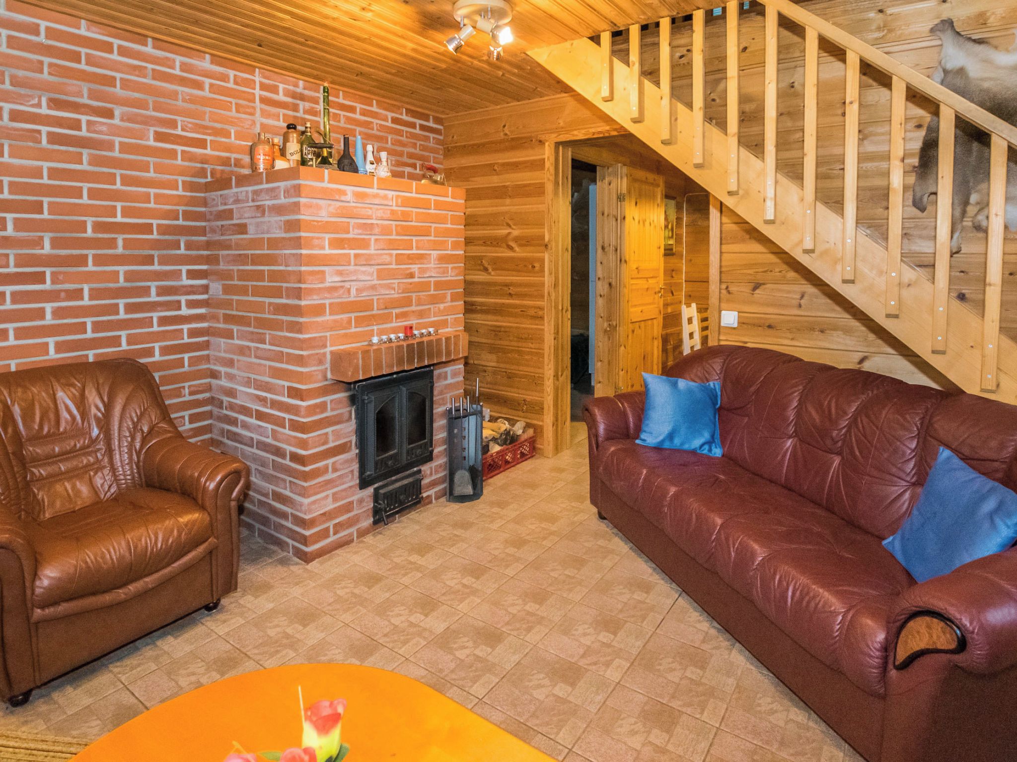 Un salon chaleureux avec une cheminée en briques, des meubles en cuir et un escalier en bois.