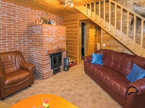 A cozy living room with a brick fireplace, leather furniture, and a wooden staircase. - Metsämökki by Interhome (Raasepori)