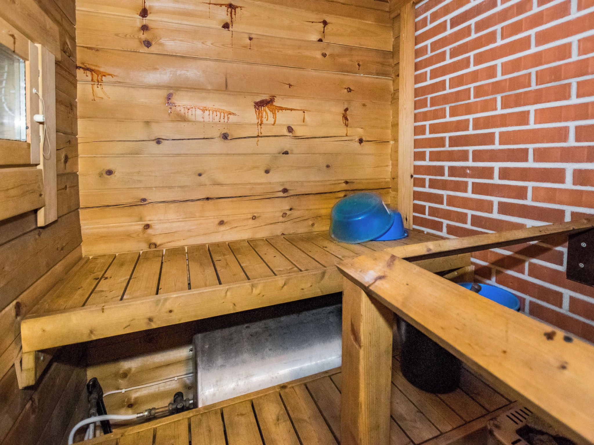 A sauna room with wooden walls and a brick wall, a bench, and a blue bucket.
