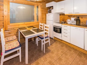 Interior de una cabaña de madera con una mesa de comedor, sillas, un refrigerador, un microondas, un horno y una cafetera.