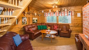 A cozy cabin interior with a wooden staircase, leather sofas, a coffee table, and deer antlers on the walls. - Metsämökki by Interhome (Raasepori)