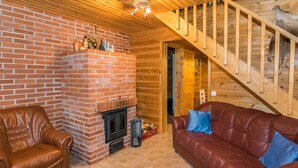 A cozy living room with a brick fireplace, leather furniture, and a wooden staircase. - Metsämökki by Interhome (Raasepori)