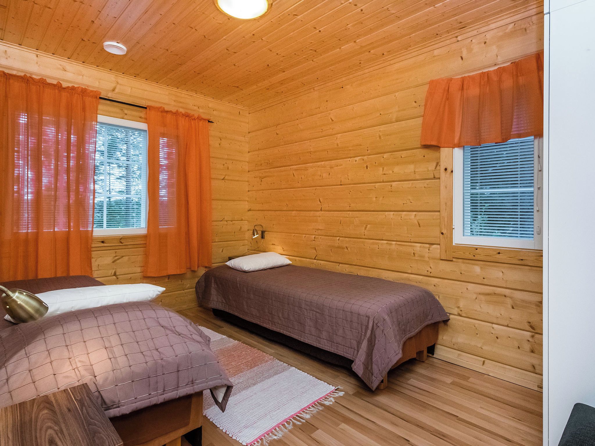 En stuga med träpanel, två sängar, ett litet bord och ett fönster med persienner.