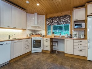 Een moderne keuken met witte kasten, een dubbele oven, een spoelbak en een raam met uitzicht op groen.