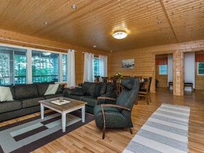 Un salon spacieux avec un plafond en bois, de grandes fenêtres, un ensemble de canapés, une table basse et un coin repas.