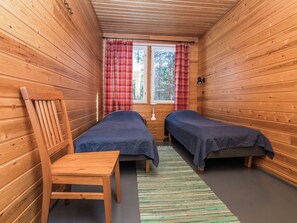 A cabin room with two beds, a chair, and a window with curtains.