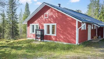 A red wooden cabin with a blue roof, white trim, and a small porch with a bench.