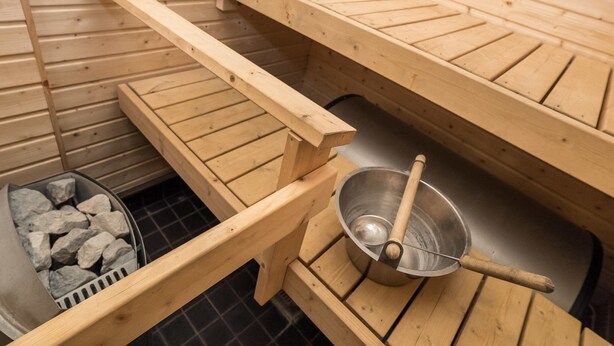 A sauna with wooden benches and a metal basin with a wooden ladle. - Rintelä 5a by Interhome (Kuusamo)