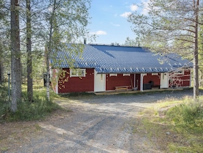 A red cabin with a blue roof, surrounded by trees, and a gravel path leading to the entrance.
