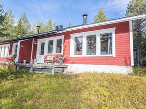 A red cabin with white trim, a deck with outdoor furniture, and a chimney.