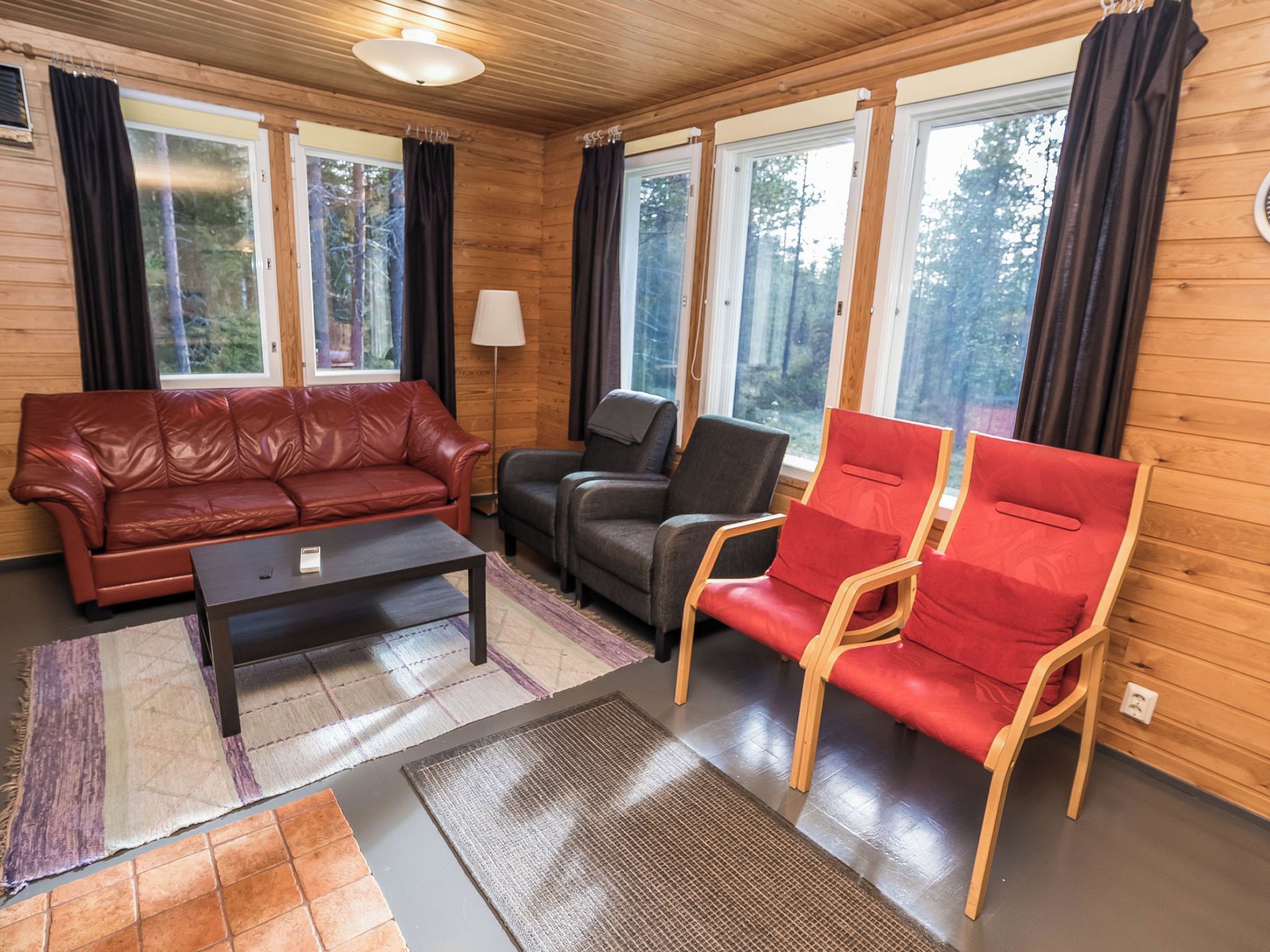 Una habitación con interior de madera, un sofá de cuero rojo, un sillón gris y una silla roja con estructura de madera.