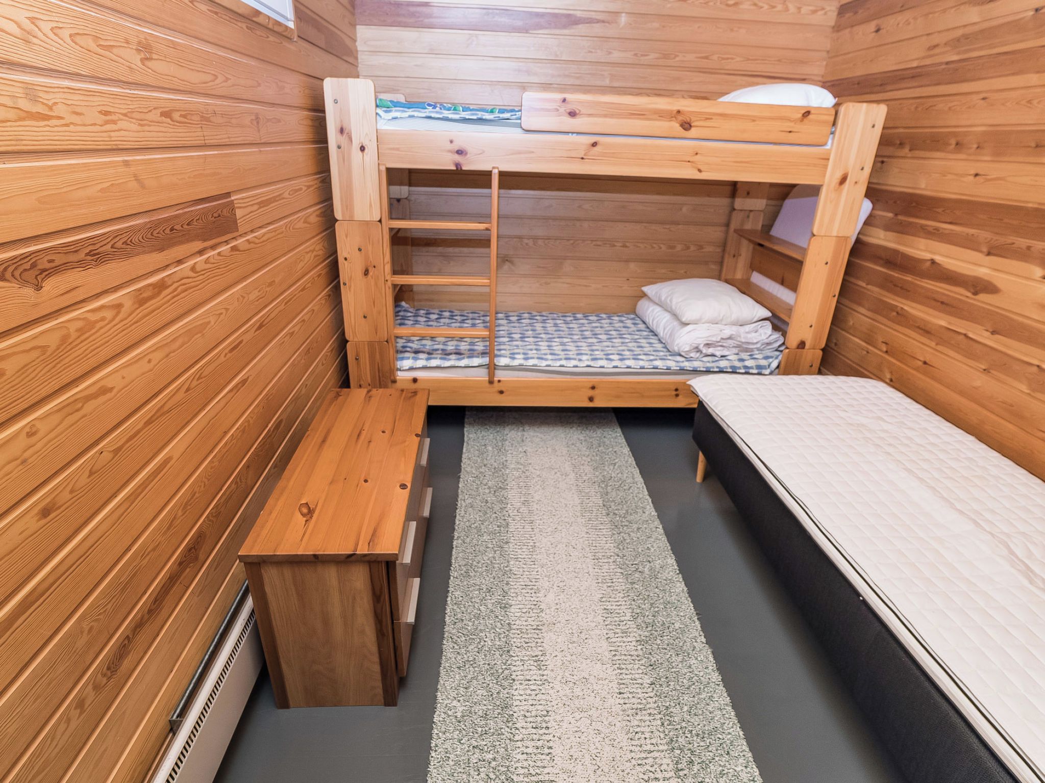 A compact wooden room with bunk beds, a small bench, and a rug.