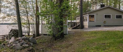 A cabin with a deck, surrounded by trees and a body of water.