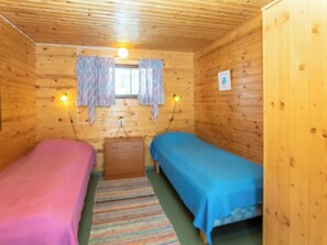 A room with two beds, wooden walls, a window with curtains, and a small wooden dresser. - Mäntyrinne by Interhome (Kerimäki)