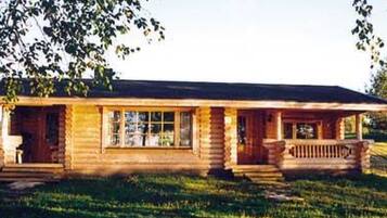 A log cabin with a porch and a front door, surrounded by a grassy yard.