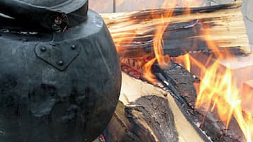 A black pot with a lid next to a fire burning wood.