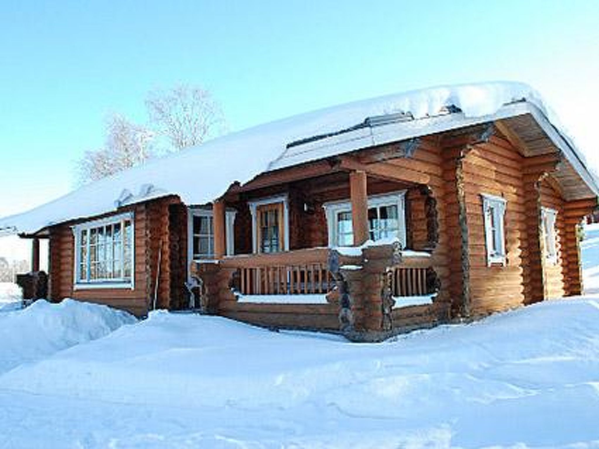 A wooden cabin with a porch and windows, surrounded by snow.