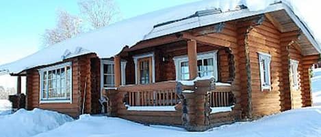 A wooden cabin with a porch and windows, surrounded by snow.