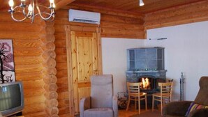 Tunnelmallinen hirsihuvilan sisustus, jossa on takka, puuseinät, televisio ja mukavat istuimet.