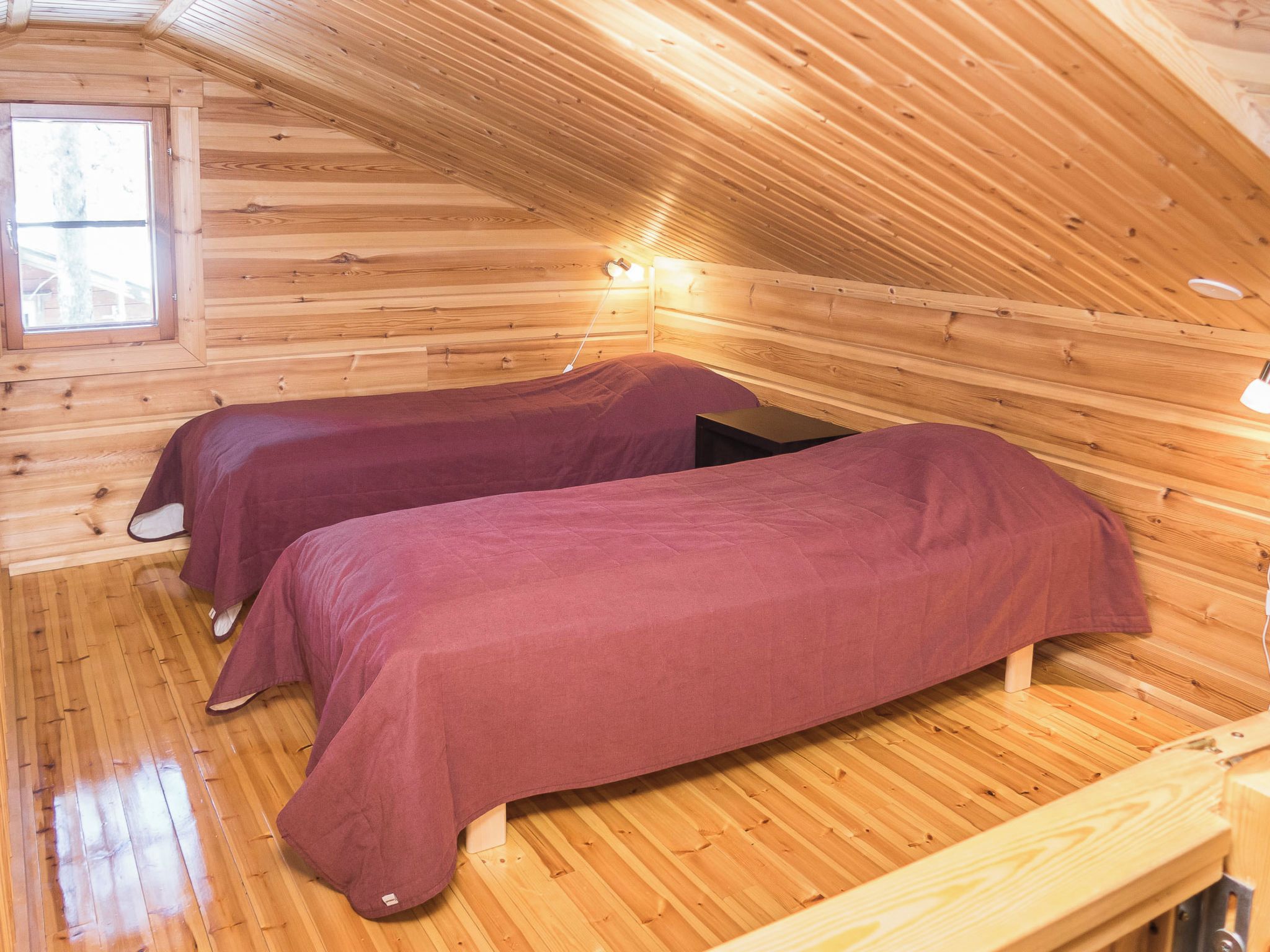 A cabin with two beds, wooden walls, a sloped ceiling, and a window.