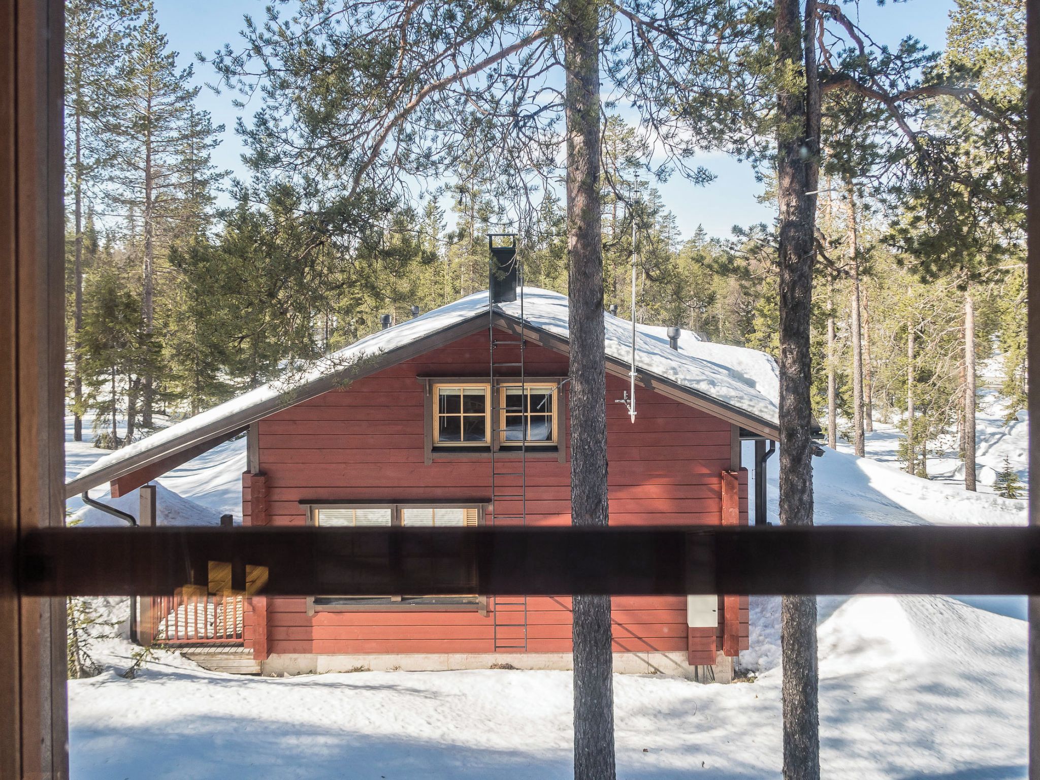 A cabin with a red exterior, a garage, and a snowy landscape with trees in the background.