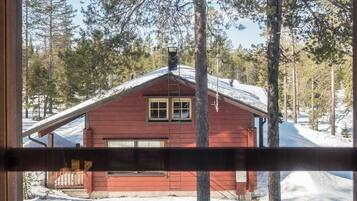Uma cabana com fachada vermelha, uma garagem e paisagem nevada com árvores ao fundo.
