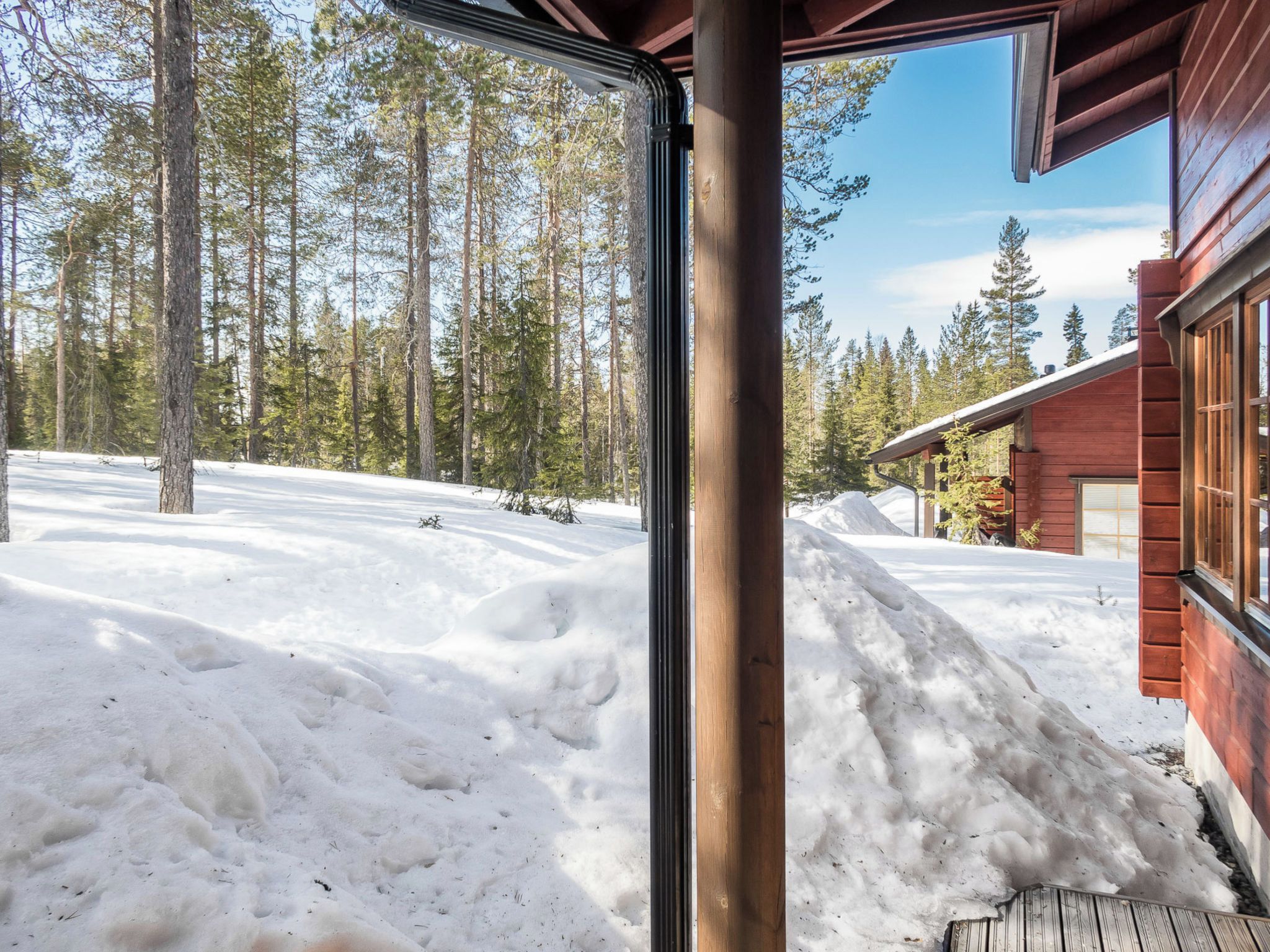 A wooden cabin with a snow-covered yard and a forest in the background.