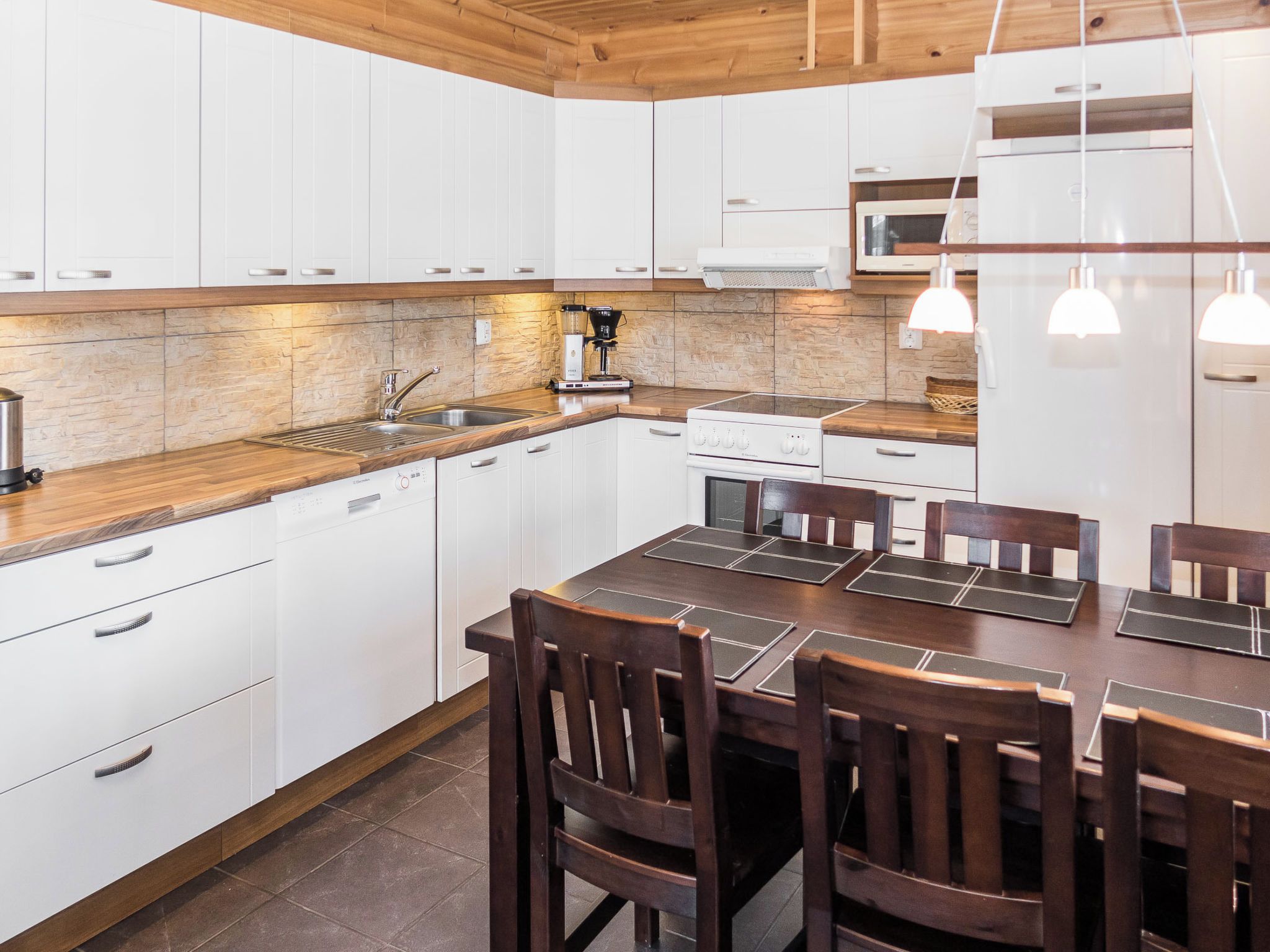 A modern kitchen with white cabinets, a wooden countertop, and a dining area with a table and chairs.