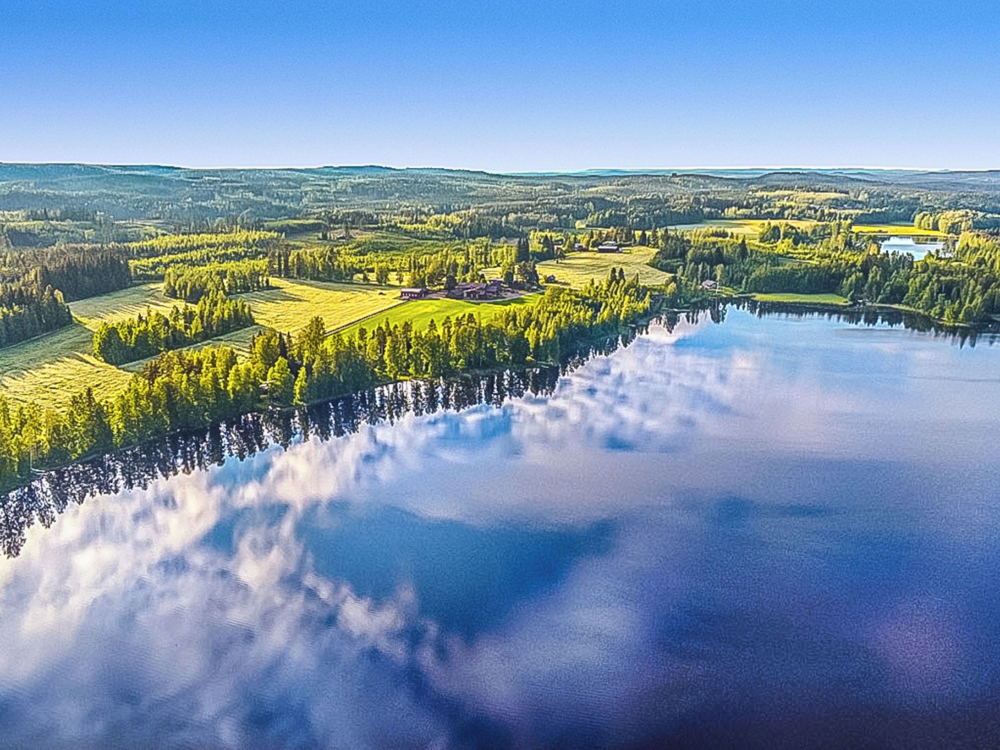 A panoramic view of a lakeside landscape with fields, trees, and a small settlement.