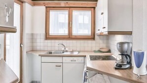 A modern kitchen with white cabinetry, a double sink, a stove, and a coffee maker. - Chalet Abendrot apARTments by Interhome (Grindelwald)