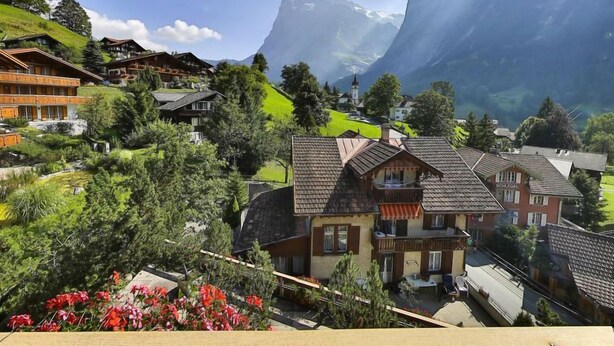 A traditional chalet-style building with a sloped roof, surrounded by lush greenery and a mountainous backdrop. - Chalet Abendrot apARTments by Interhome (Grindelwald)